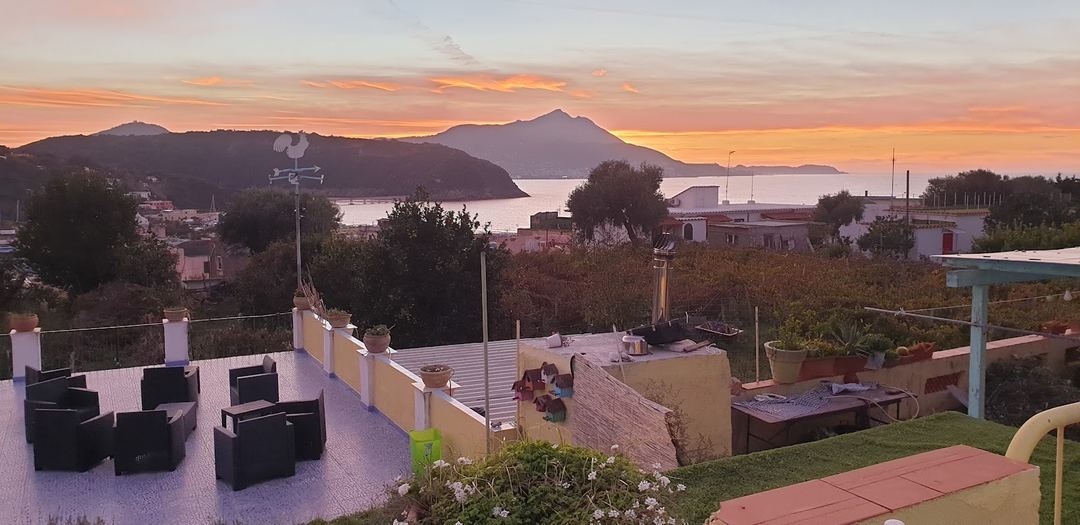 Sunset view from the B&B terrace overlooking a coastal bay with mountains and volcanic peaks in the distance.