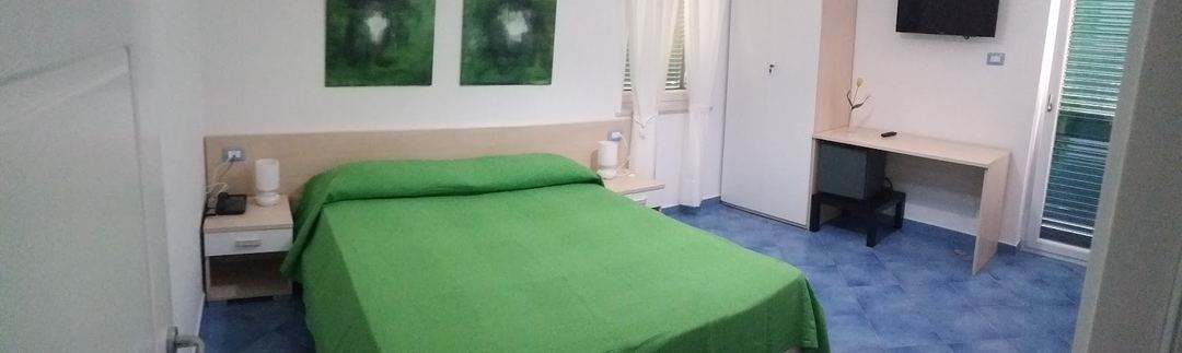 A hotel bedroom with bright green bedding, wooden headboard, and blue flooring.